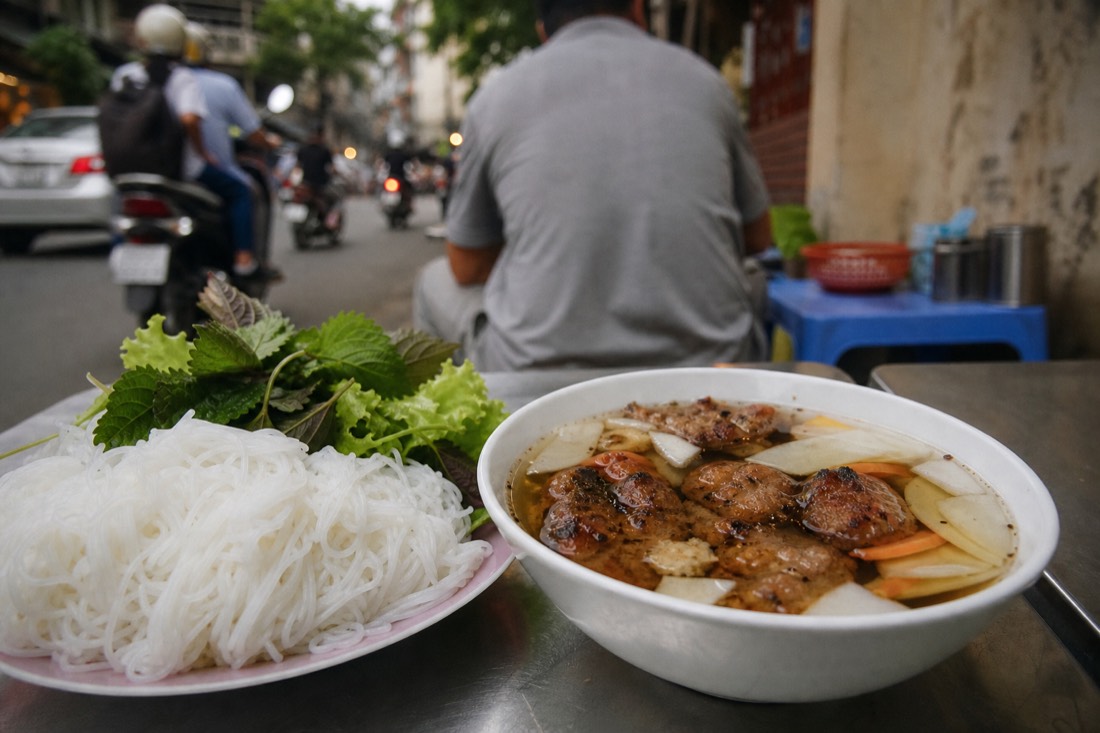 Bowl of bun cha dipping broth with grilled pork and pickled papaya on a Hanoi restaurant table
