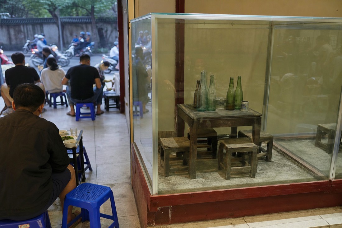 Glass display case preserving a restaurant table and stools inside a Hanoi bun cha shop