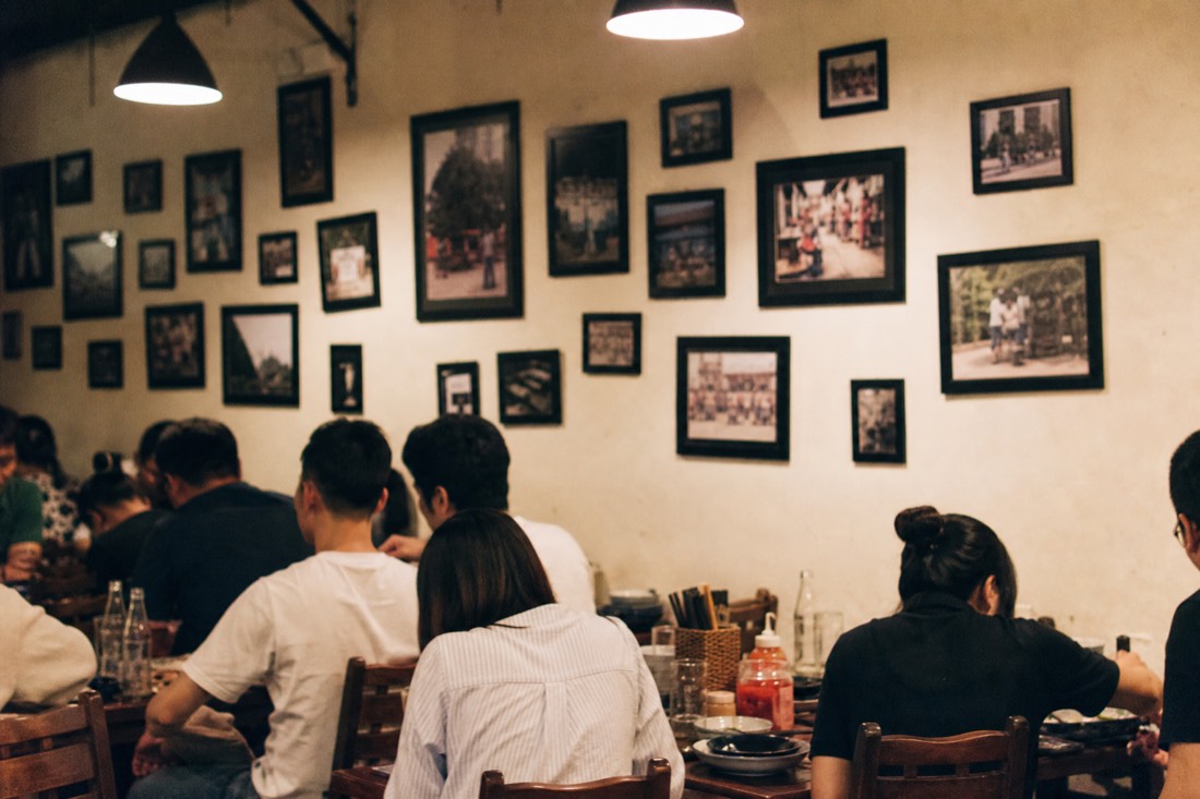 Wall of small framed photographs above tables inside a well-known Hanoi bun cha restaurant