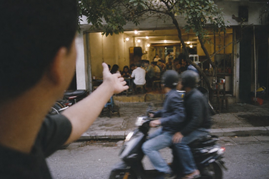 Local guide gesturing toward a busy bun cha restaurant entrance in Hanoi