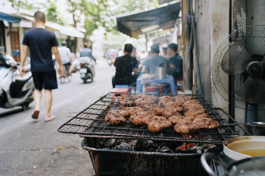 Charcoal grill loaded with pork patties outside a busy Hanoi bun cha shop at lunchtime