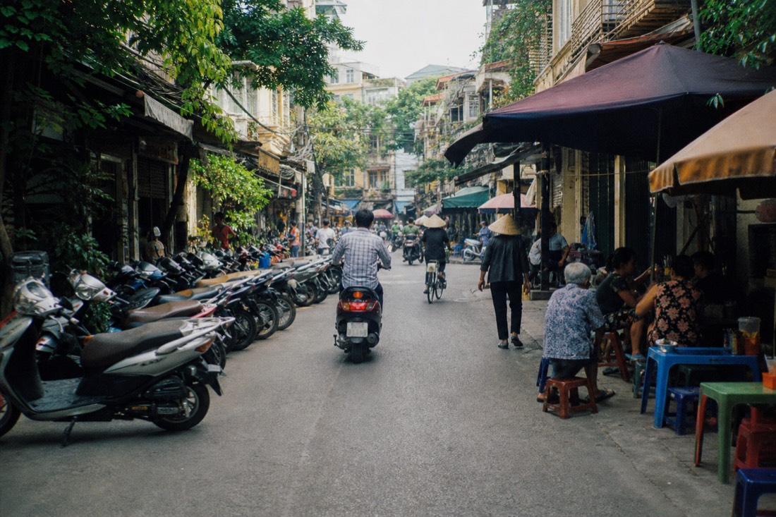 Busy narrow Hanoi Old Quarter street packed with parked motorbikes and food stalls in daylight