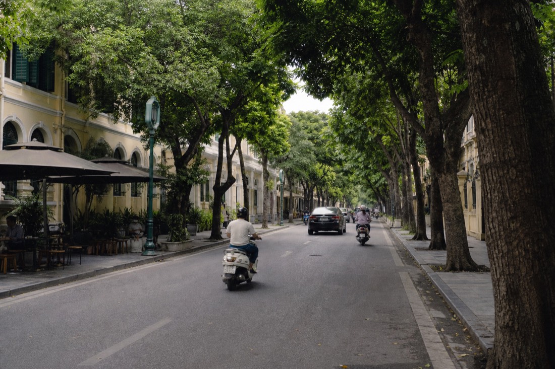 Wide tree-lined French Quarter boulevard in Hanoi with colonial-era buildings and outdoor cafe tables
