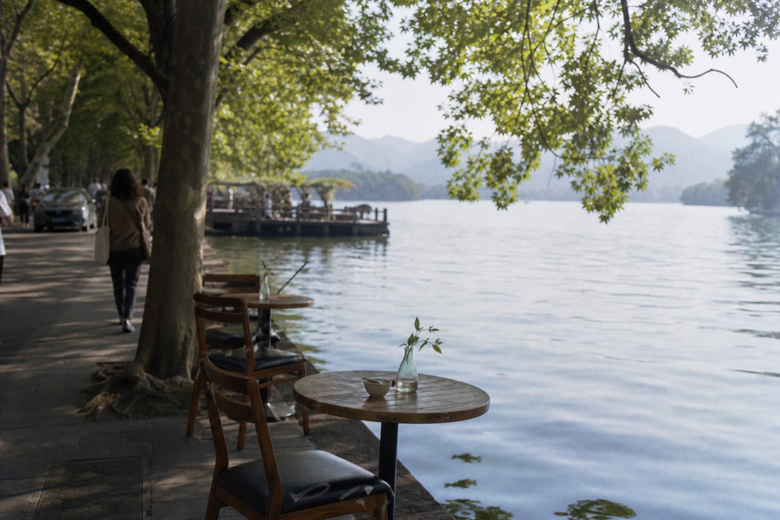 West Lake shoreline path in Tay Ho with cafe tables overlooking calm water in soft morning light