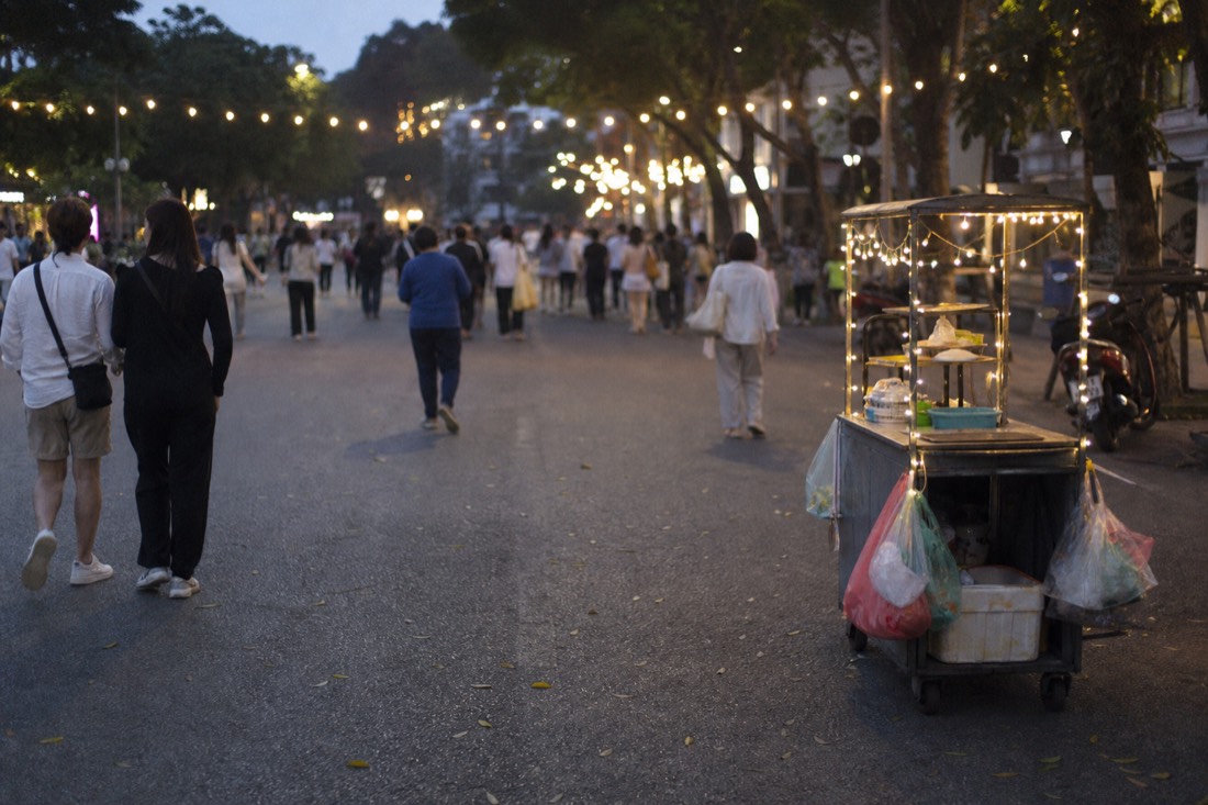 Pedestrian street around Hoan Kiem Lake in the evening with strolling crowds and a food vendor cart